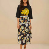 Full body view of a model styling the black Farm Rio graphic t-shirt with a patterned midi skirt