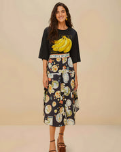 Full body view of a model styling the black Farm Rio graphic t-shirt with a patterned midi skirt