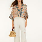 Model wearing Farm Rio soft pink floral delhi tapestry bodysuit paired with white trousers, full length view.