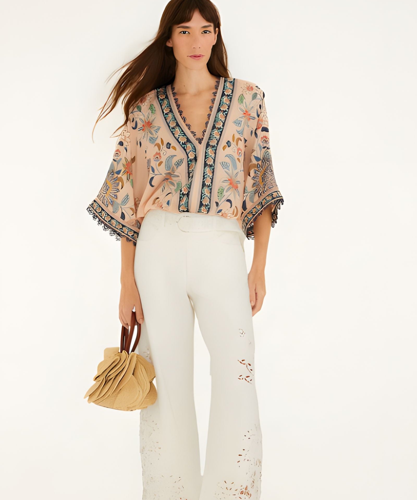Model wearing Farm Rio soft pink floral delhi tapestry bodysuit paired with white trousers, full length view.
