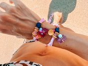 Close-up of a person's wrist two GOUPI bandana wrap bracelets, eaturing the fuchsia and lilac glass crab charms with 24k gold-plated accents