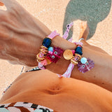 Close-up of a person's wrist two GOUPI bandana wrap bracelets, eaturing the fuchsia and lilac glass crab charms with 24k gold-plated accents
