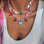 Close-up of a person wearing a colorful beaded necklace and a pink bandana necklacer with a star charm. Jewellery Layering at it best. 
