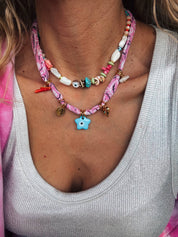 Close-up of a person wearing a colorful beaded necklace and a pink bandana necklacer with a star charm. Jewellery Layering at it best. 