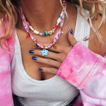 Person wearing a colorful beaded necklace and pink bandance necklace by Greek brand Goupi.