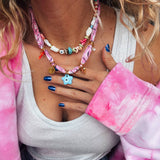 Person wearing a colorful beaded necklace and pink bandance necklace by Greek brand Goupi.
