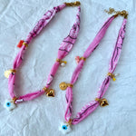 A stacked pile of colorful handmade GOUPI pink bandana necklaces, ready for dispatch from Greece