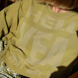 A close-up view of the khaki cotton fleece fabric showing the faded mineral wash texture and the bold cream graphic text print.