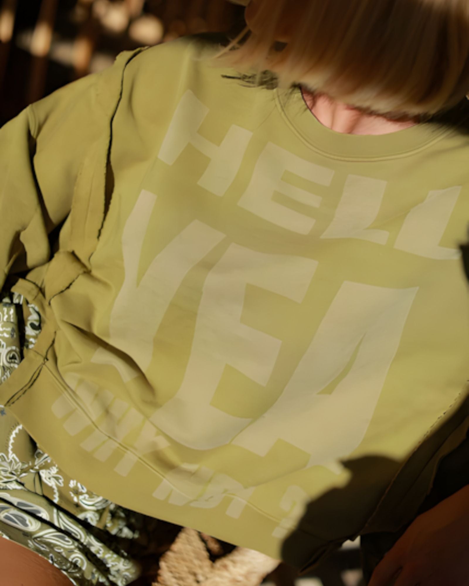 A close-up view of the khaki cotton fleece fabric showing the faded mineral wash texture and the bold cream graphic text print.