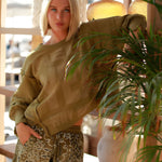 A blonde woman wearing the oversized khaki green Judy graphic sweatshirt with a tonal print, styled with matching paisley print shorts.