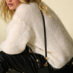 Lifestyle shot of the black Nathan vegan leather strap worn crossbody with a white knit sweater
