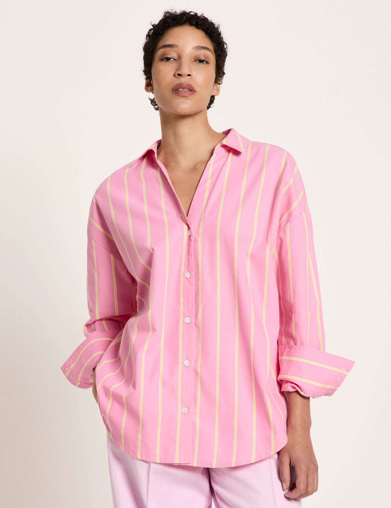 Woman wearing the bright orchid and sun yellow striped cotton shirt, highlighting the relaxed open neckline and wide buttoned cuffs.
