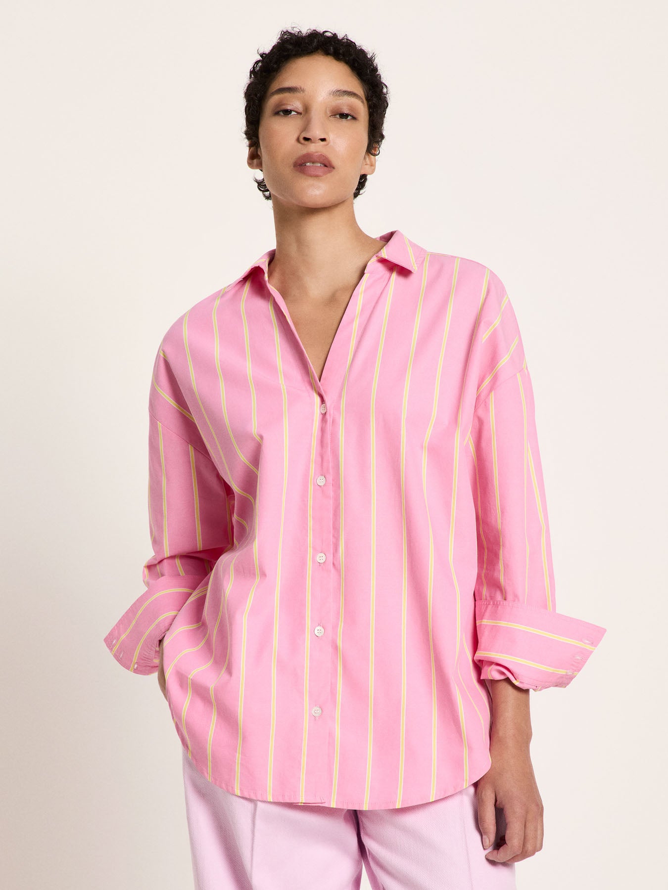 Woman wearing the bright orchid and sun yellow striped cotton shirt, highlighting the relaxed open neckline and wide buttoned cuffs.