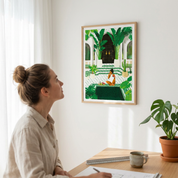 Woman at a desk looking at the Medina Oasis Moroccan riad poster in a wood frame on a white wall.