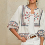 Close-up view of the red and blue geometric floral embroidery on a white Mabe Apparel cotton jacket.