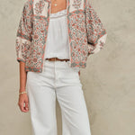 Model wearing an open-front Mabe Apparel artisan floral print jacket with white pants and jewelry.