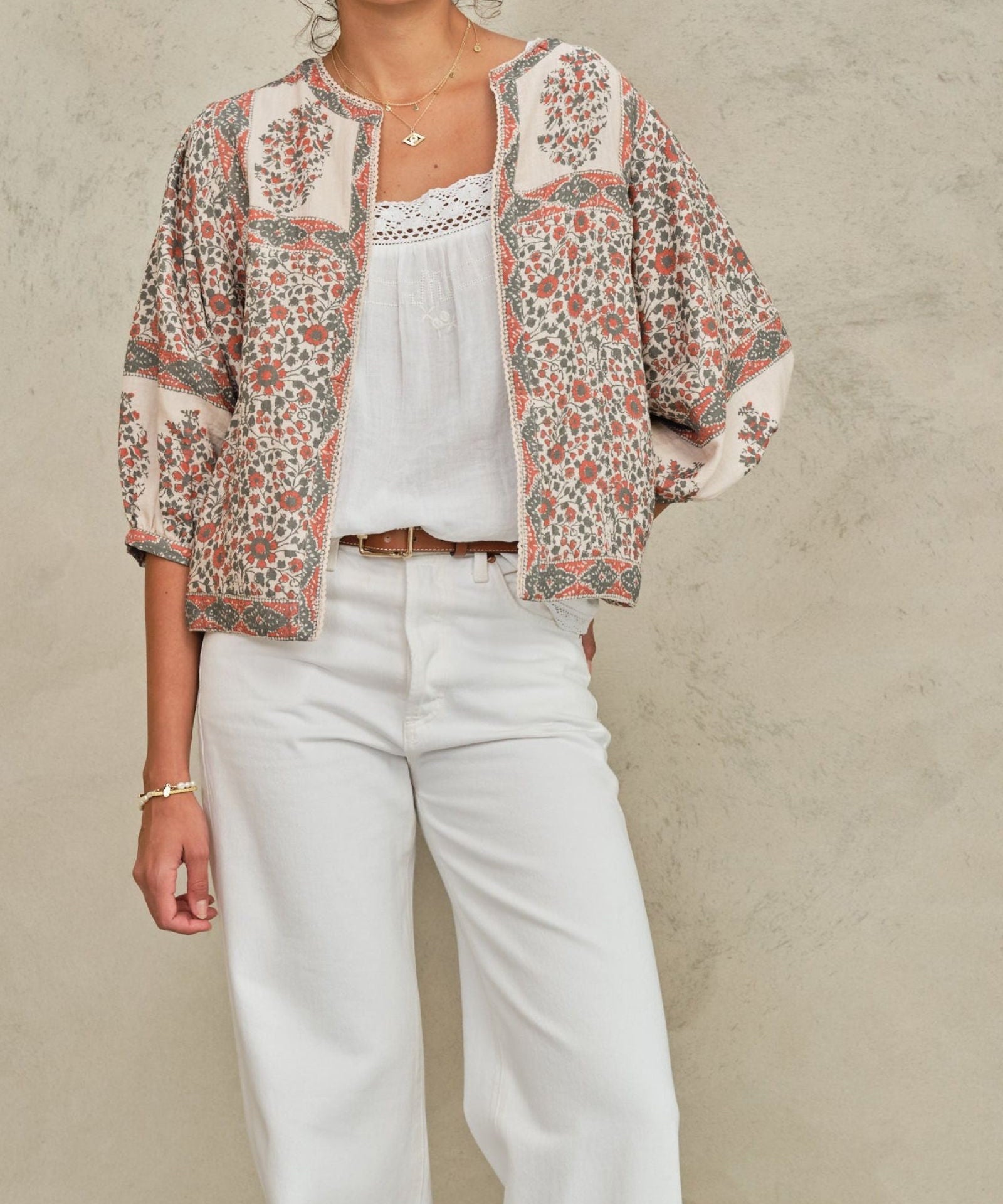 Model wearing an open-front Mabe Apparel artisan floral print jacket with white pants and jewelry.