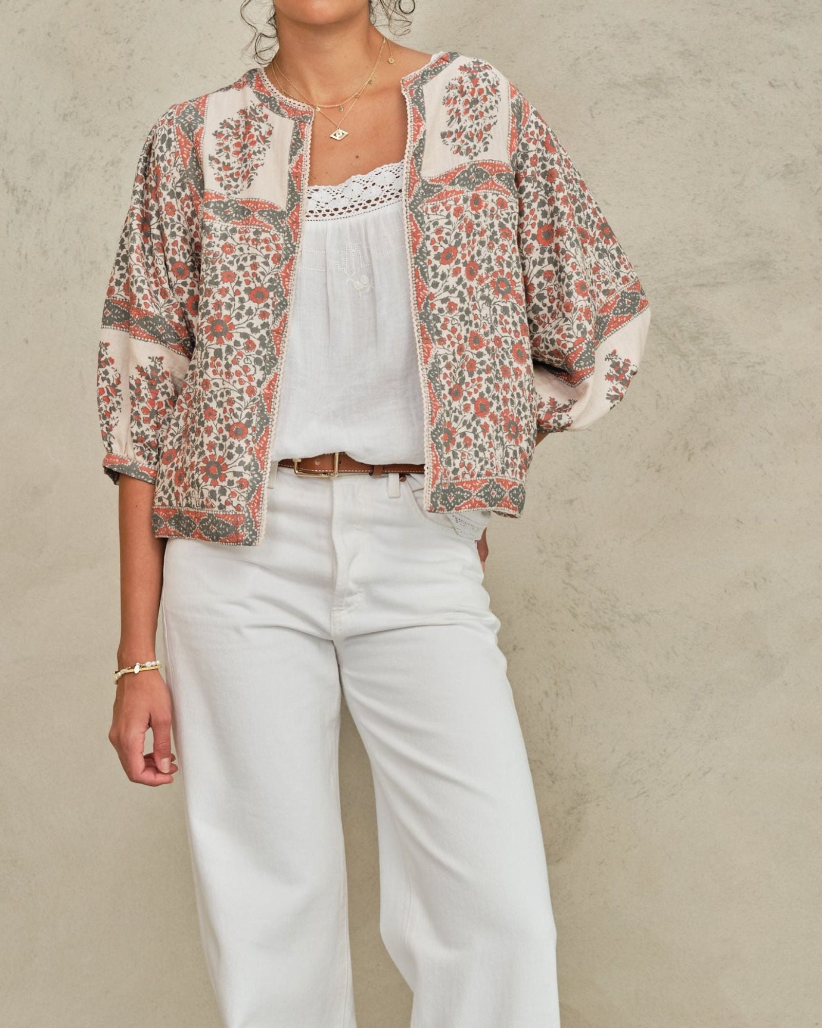 Model wearing an open-front Mabe Apparel artisan floral print jacket with white pants and jewelry.