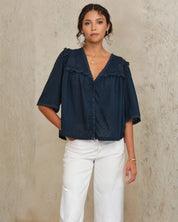 Model wearing Mabe Apparel navy embroidered cotton blouse with white trousers and jewelry.