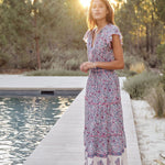 Woman in a Mabe Apparel Della resort maxi dress in blue and pink floral print with flutter sleeves.