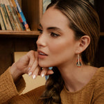 A woman wearing Mayana Designs handwoven turquoise and orange beaded feather earrings, showcasing their elegant lightweight design