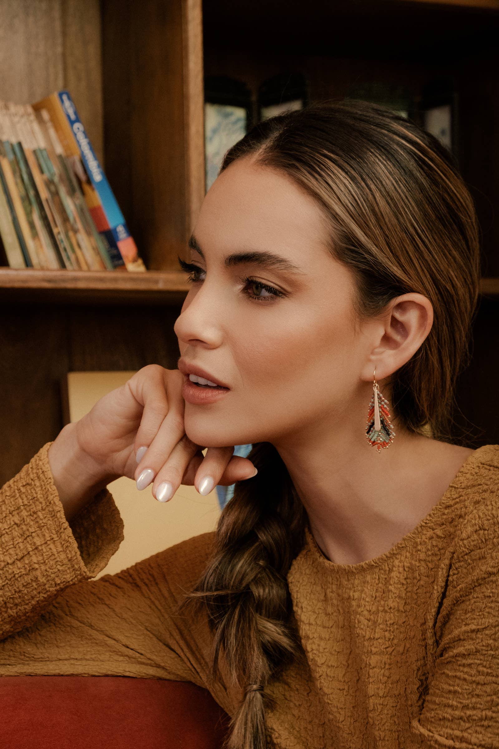 A woman wearing Mayana Designs handwoven turquoise and orange beaded feather earrings, showcasing their elegant lightweight design