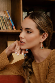 A woman wearing Mayana Designs handwoven turquoise and orange beaded feather earrings, showcasing their elegant lightweight design