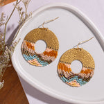lose-up of Mayana Designs Earth Ombre Fringe Disk Earrings, highlighting the intricate beaded fringe in ombre colors and hammered brass arch.