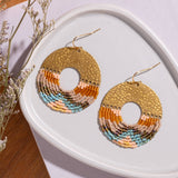 lose-up of Mayana Designs Earth Ombre Fringe Disk Earrings, highlighting the intricate beaded fringe in ombre colors and hammered brass arch.