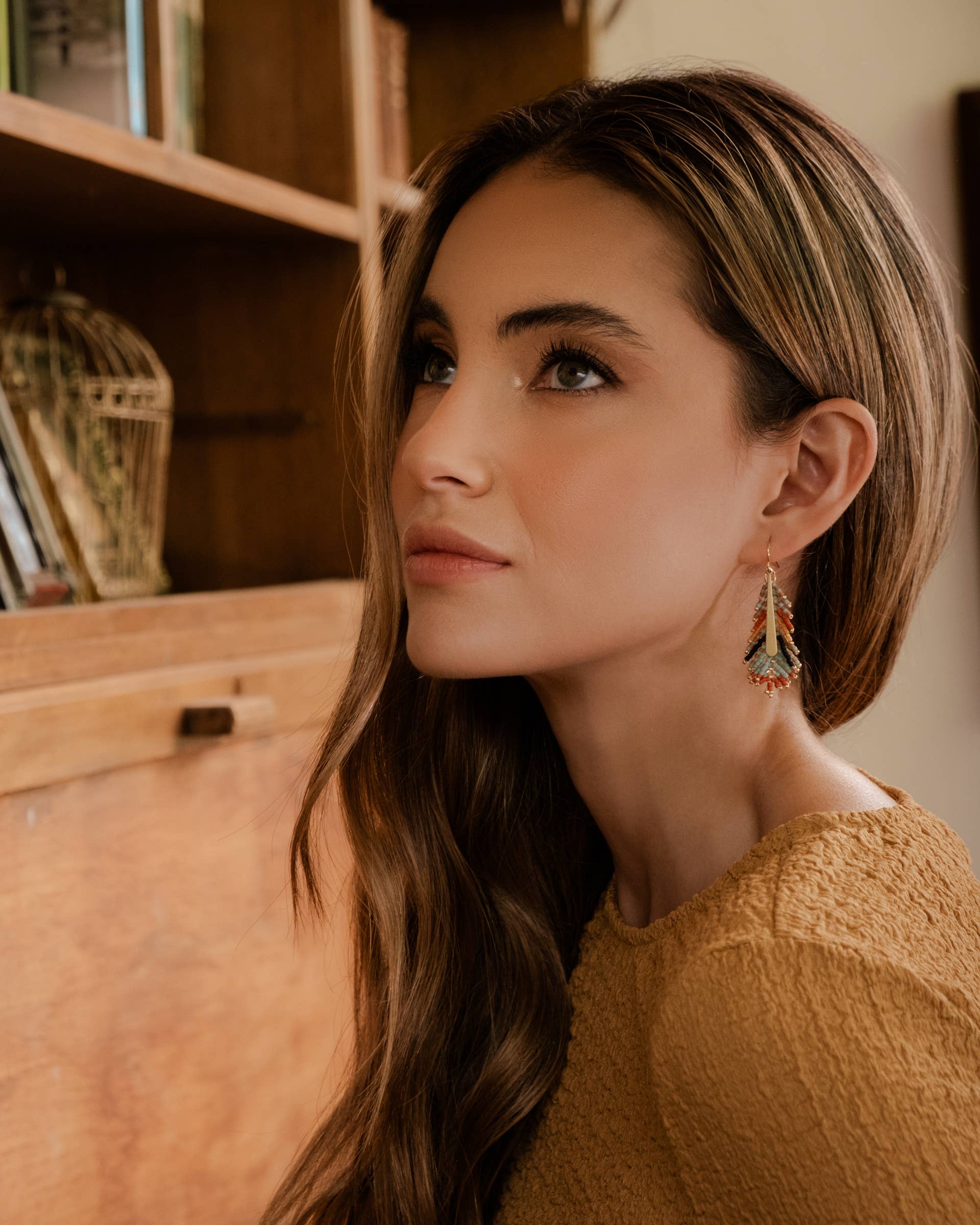 Close-up of a woman styling Mayana Designs artisan-crafted feather earrings in turquoise and orange highlighting their intricate beadwork
