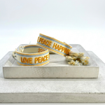 Cream woven Parsley & Pepper bracelet with mustard-yellow “LOVE PEACE HAPPINESS” embroidery, yellow and light blue borders – detail.
