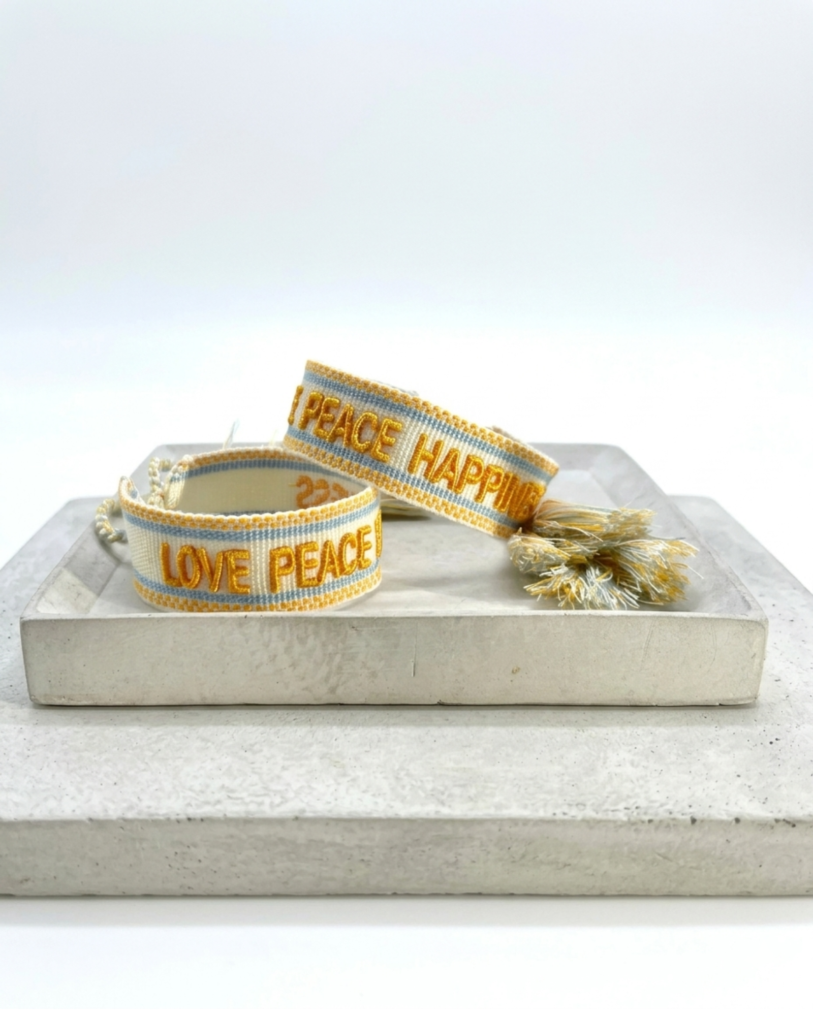 Cream woven Parsley & Pepper bracelet with mustard-yellow “LOVE PEACE HAPPINESS” embroidery, yellow and light blue borders – detail.