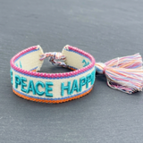 Close-up of adjustable woven turquoise friendship bracelet with embroidered “LOVE PEACE HAPPINESS” lettering and sliding knot tassel cords.