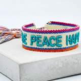 Close-up of adjustable woven turquoise friendship bracelet with embroidered “LOVE PEACE HAPPINESS” lettering and sliding knot tassel cords.
