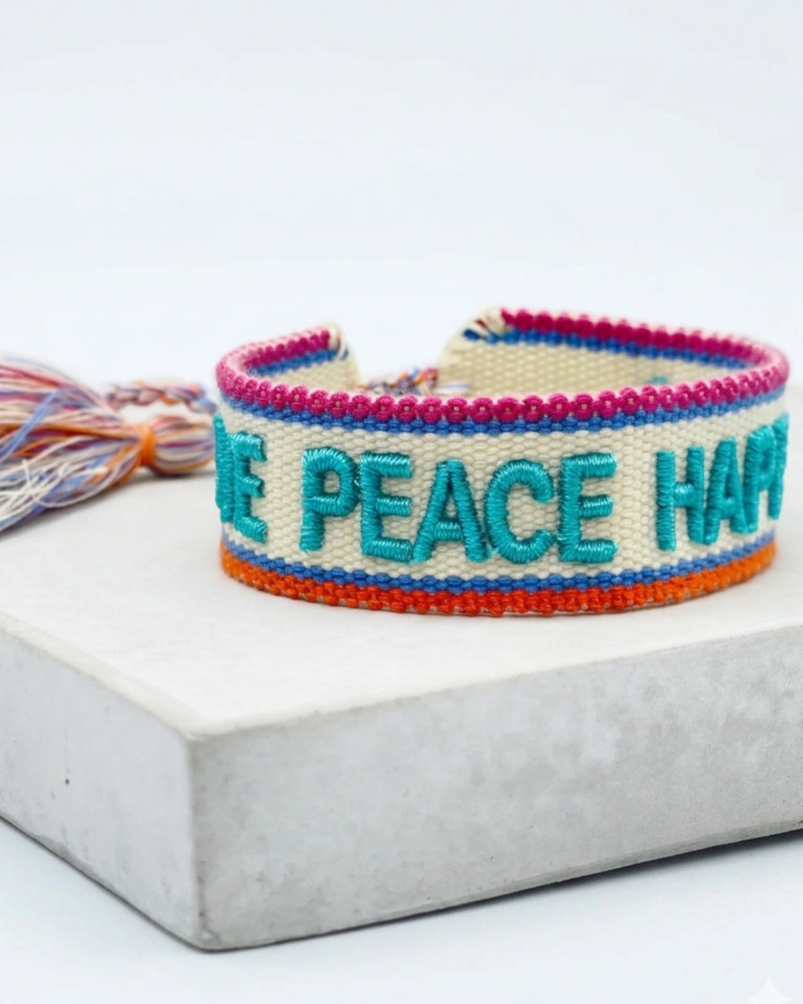 Close-up of adjustable woven turquoise friendship bracelet with embroidered “LOVE PEACE HAPPINESS” lettering and sliding knot tassel cords.