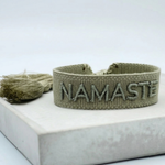 Close-up of adjustable sage eucalyptus woven bracelet with tone-on-tone embroidered “NAMASTE” lettering and sliding knot tassel cords.