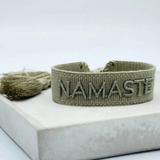 Close-up of adjustable sage eucalyptus woven bracelet with tone-on-tone embroidered “NAMASTE” lettering and sliding knot tassel cords.