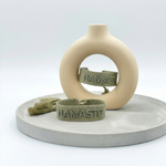 Close-up of adjustable sage eucalyptus woven bracelet with tone-on-tone embroidered “NAMASTE” lettering and sliding knot tassel cords.