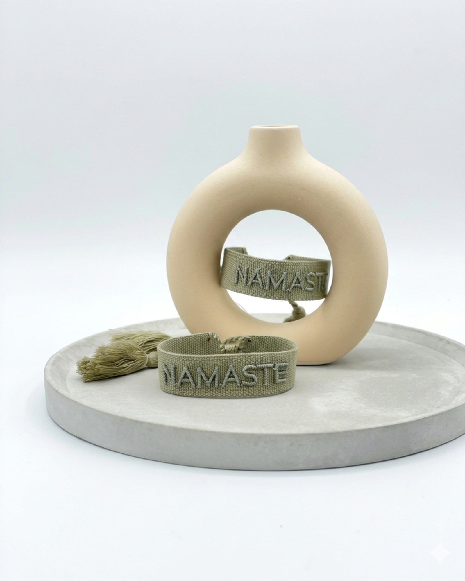 Close-up of adjustable sage eucalyptus woven bracelet with tone-on-tone embroidered “NAMASTE” lettering and sliding knot tassel cords.