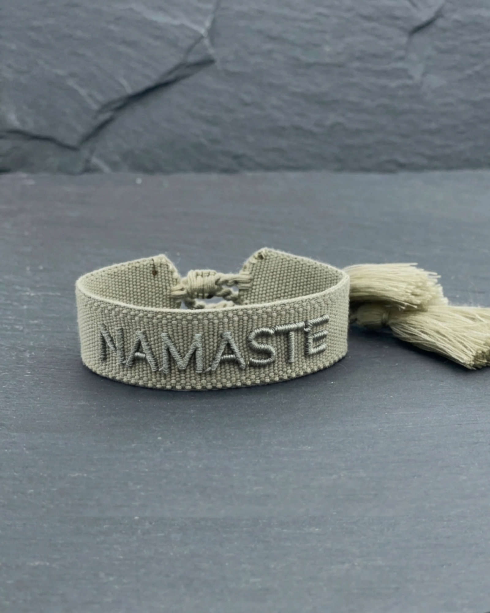 Close-up of adjustable sage eucalyptus woven bracelet with tone-on-tone embroidered “NAMASTE” lettering and sliding knot tassel cords.