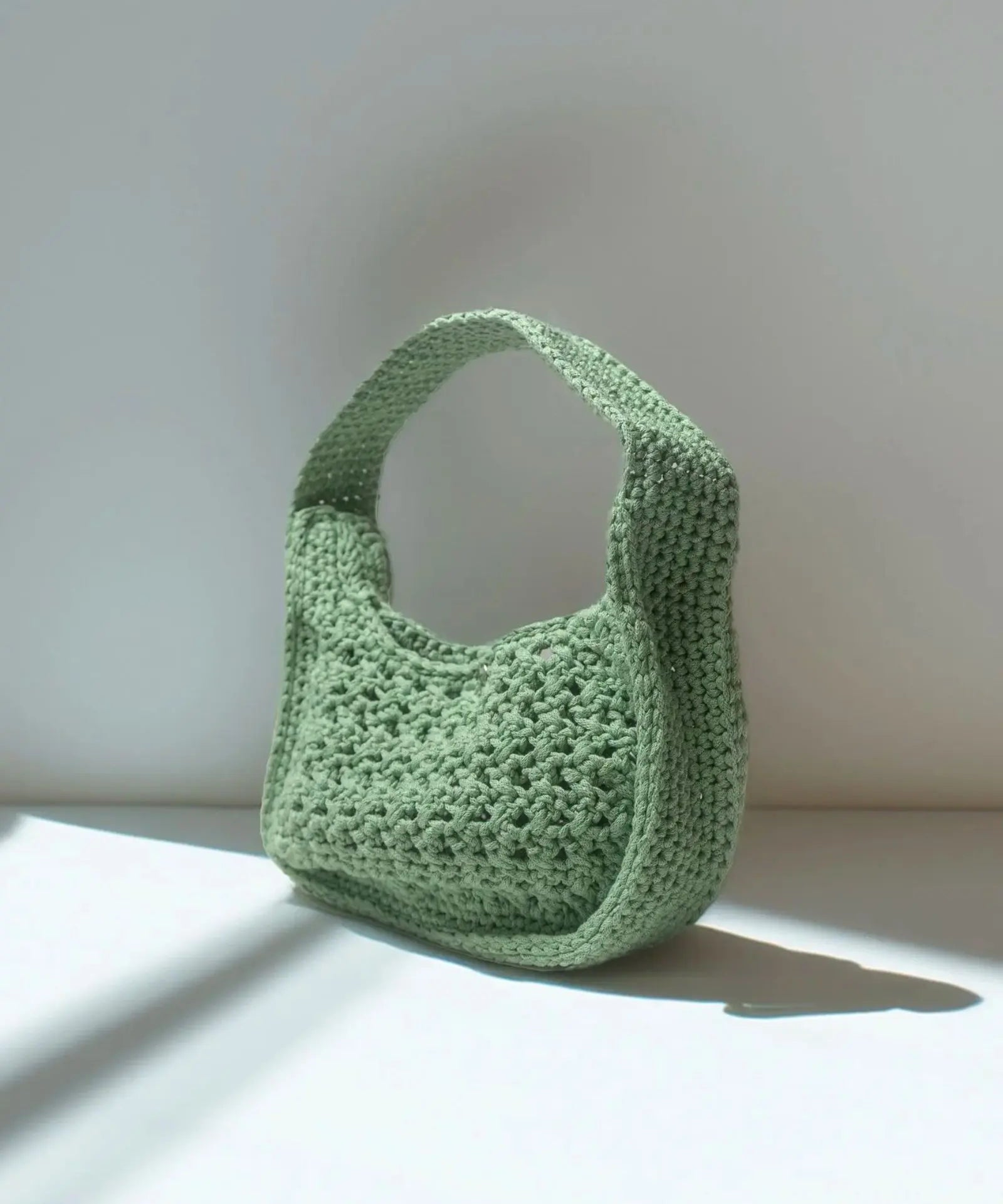 Riviera Lili handcrafted crochet bag in sage green standing in natural light with shadow — Atelier Bagatelle Switzerland