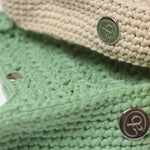 Close-up detail of Atelier Bagatelle's Riviera Lili crocheted bags in sage green and natural beige with logo