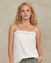 Close-up view of a model wearing a Mabe Apparel white embroidered cotton tank top with gold jewelry.