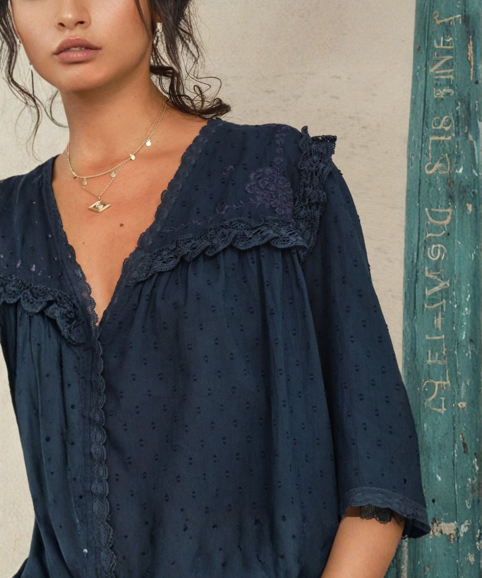 Close-up of the scalloped lace trim and floral embroidery on a Mabe Apparel navy blue blouse.