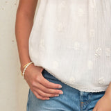Close-up of the textured tufted dots and lace trim hem on a white Mabe Apparel cotton camisole.
