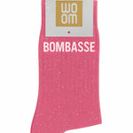 Bubble gum pink glitter message socks with a white jacquard BOMBASSE inscription at the ankle, presented in their original Woom paper packaging.