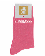 Bubble gum pink glitter message socks with a white jacquard BOMBASSE inscription at the ankle, presented in their original Woom paper packaging.