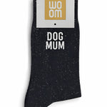 Black glitter message socks with a white jacquard DOG MUM inscription at the ankle, presented in their original Woom paper packaging.