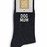 Black glitter message socks with a white jacquard DOG MUM inscription at the ankle, presented in their original Woom paper packaging.