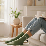 Cozy indoor lifestyle shot of a model relaxing on a couch, styling the almond green glitter message socks with casual home attire.
